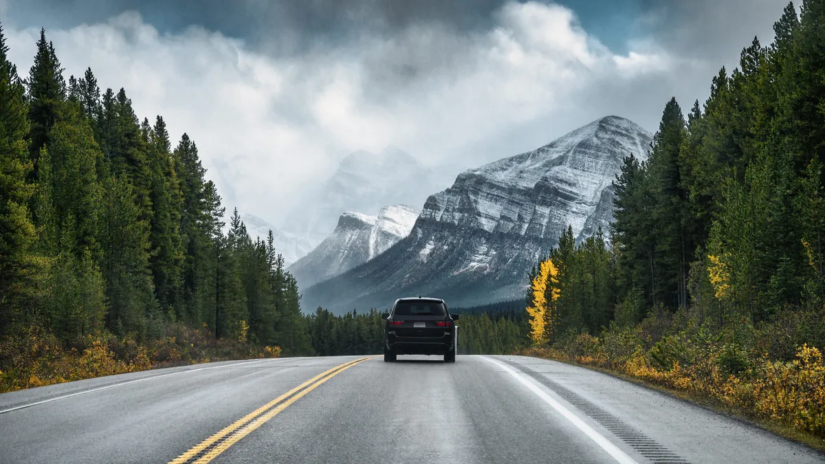 Image of back of car on a road headed toward large snow-capped mountains