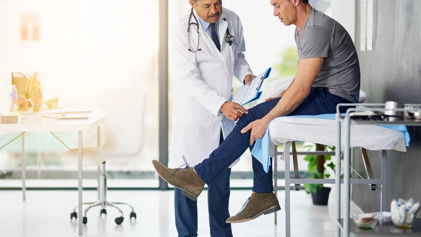 A doctor checks the knee of a patient seated on an examination table.
