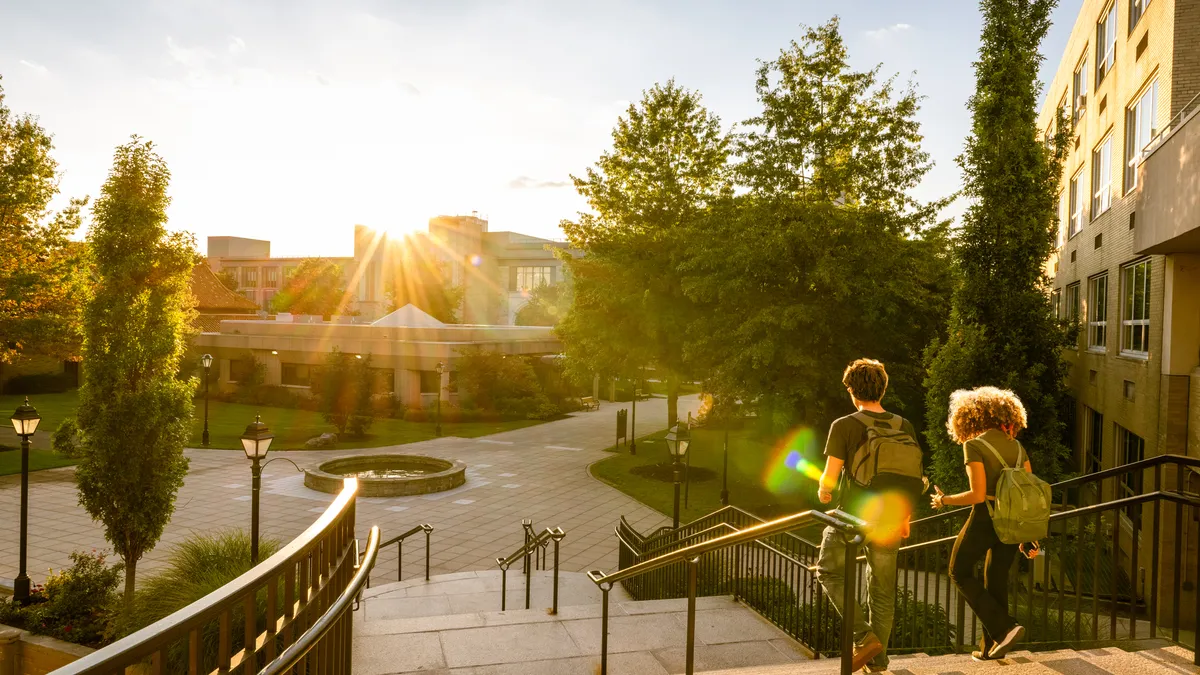 Rear view of two university students walk down campus stairs at sunset