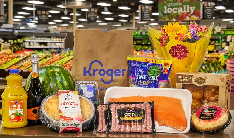 Grocery items including quiche, orange juice, a floral bouquet and sweet kale, on a table at a grocery store.