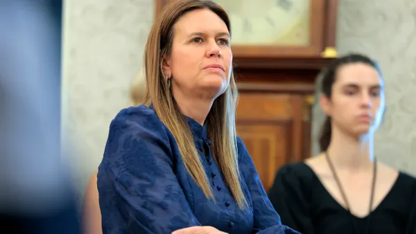 A person stands with arms crossed as another person looks on.