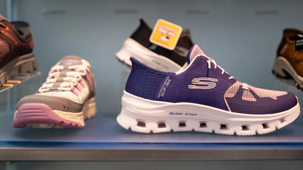 A closeup of a store display. A grey and pink Skechers sneaker is seen next to a purple Skechers sneaker.