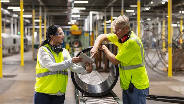Two people standing face to face on a plastics production line.