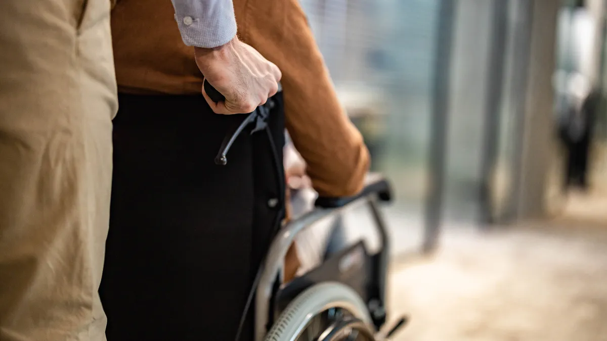 A hand pushes someone in a wheelchair