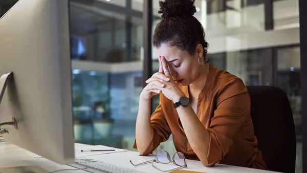 Person sitting at a desk with her hands on their forehead.