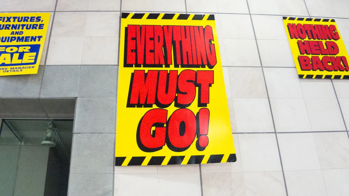 Three signs plastered to a grey tiled wall announce a store liquidation sale, with the middle one saying that "Everything must go!"