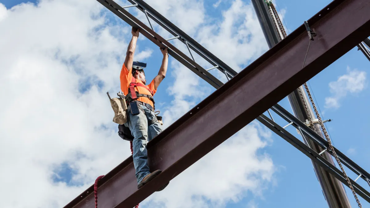 a worker in an orange vet sits stop a steel beam