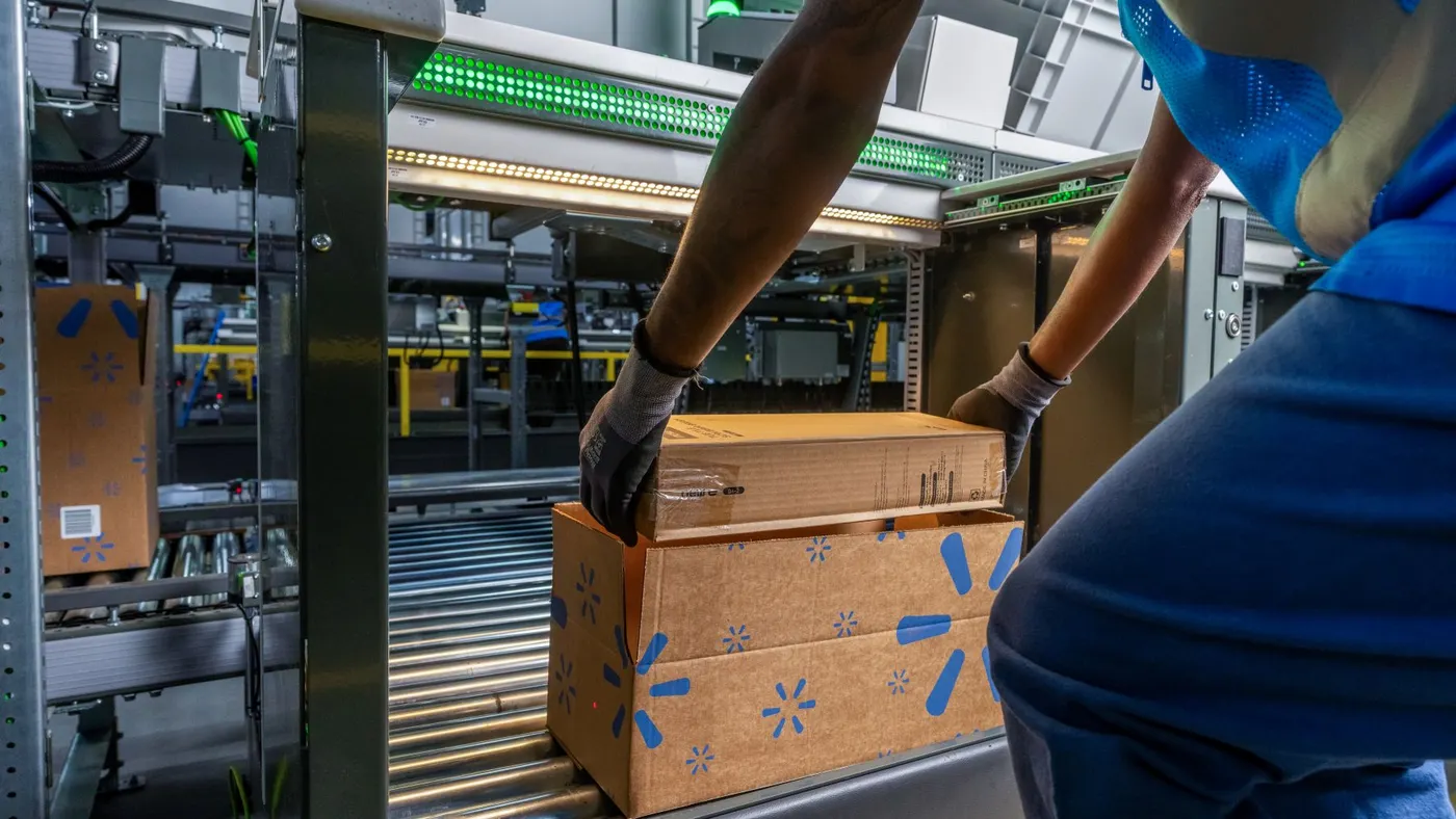 A Walmart worker lifts a box off a conveyer belt.
