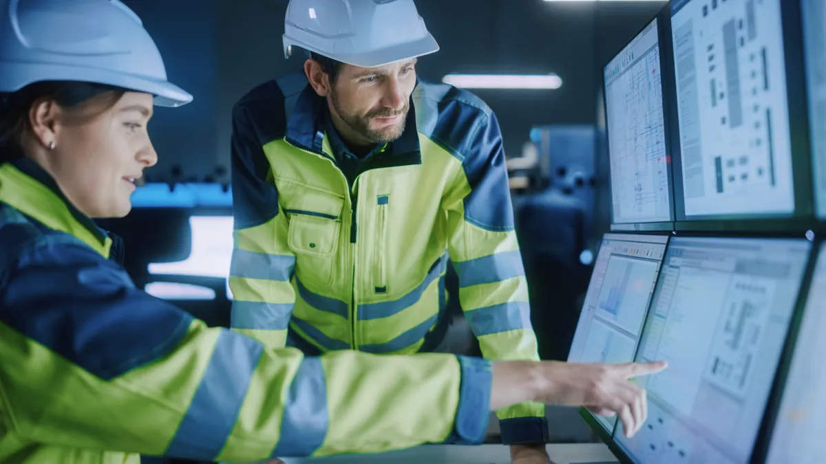 A project engineer talks to a computer operator who points to screens showing AI and machine learning enhanced tools.