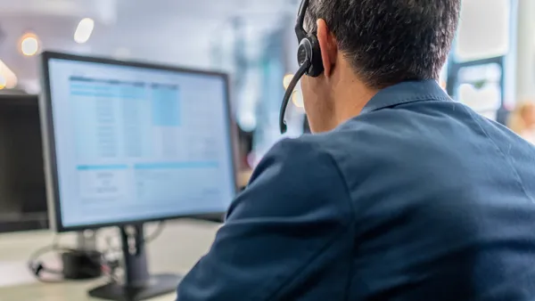 Close-up of customer service representative wearing wireless headset working on desktop computer in call center.