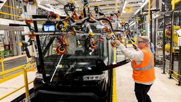 An employee in an orange vest pulls a machine down to help assemble a vehicle, which is on the production line.