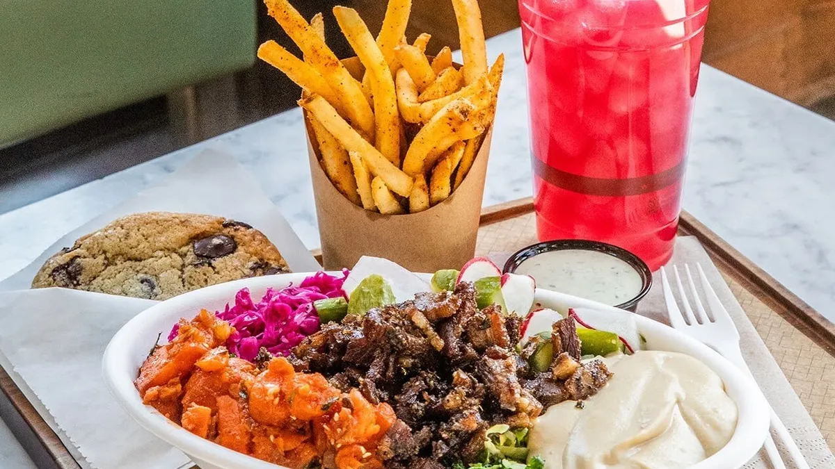 An image of a bowl with meat and other vegetables. A cookie is next to the bowl as is a plastic fork and pink drink.