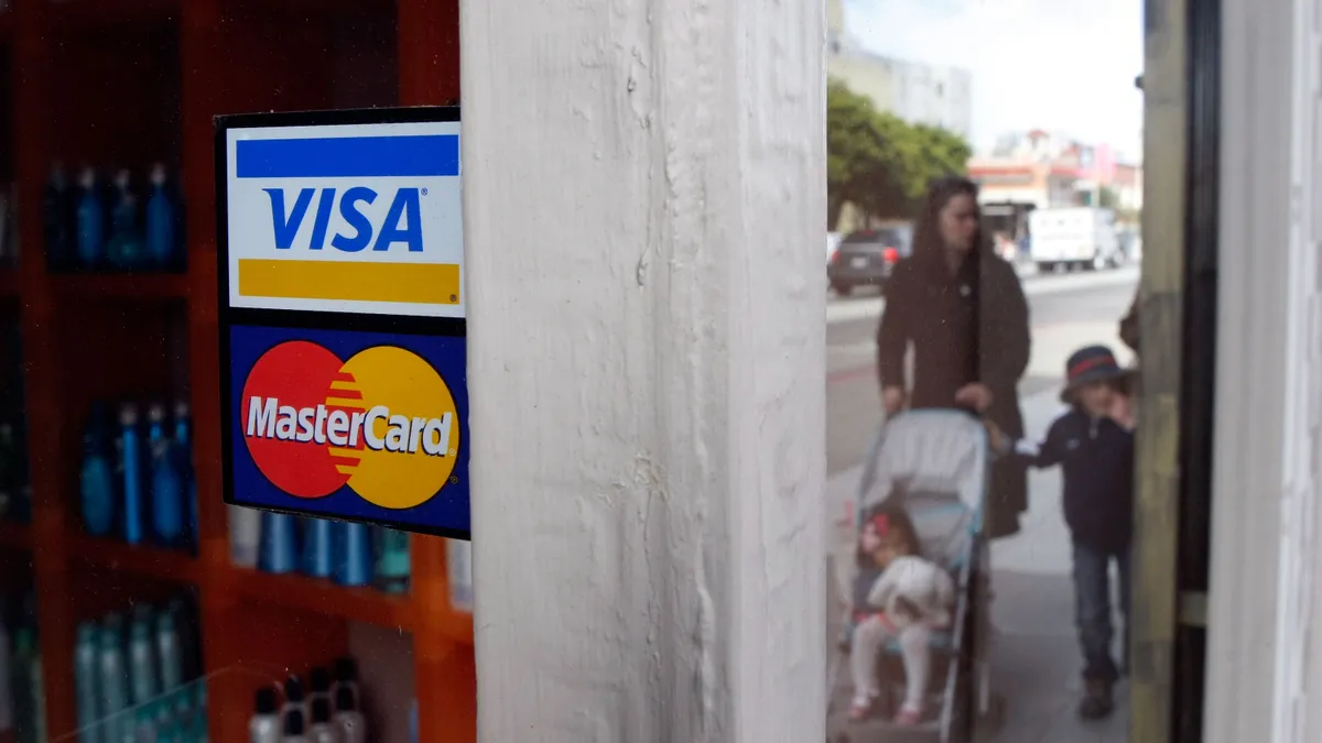 Stickers with the visa and mastercard logos on the exterior window of a store.