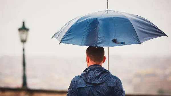 Rainy day. Young man is holding blue umbrella and walking in rain.