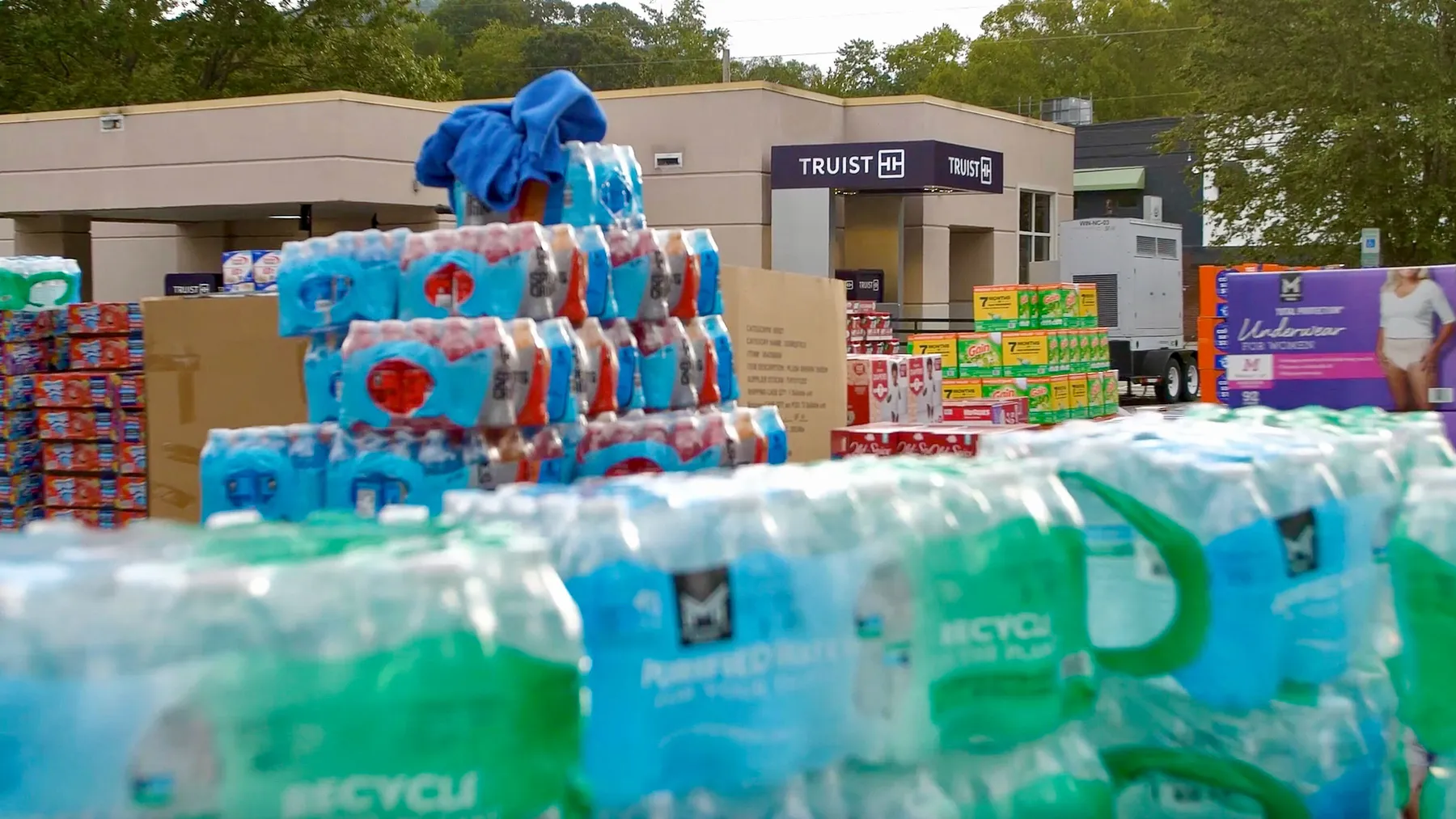 Bottled water and other supplies are stacked in the foreground with a Truist branch location in the background.