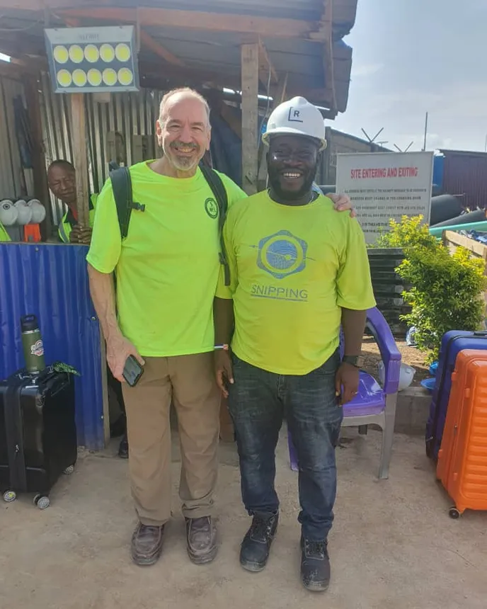 Two men in hard hats stand in front of a construction site