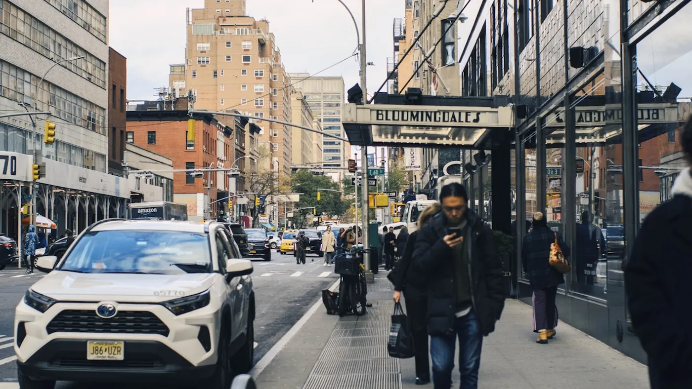 People walking down the street and cars driving in a city.