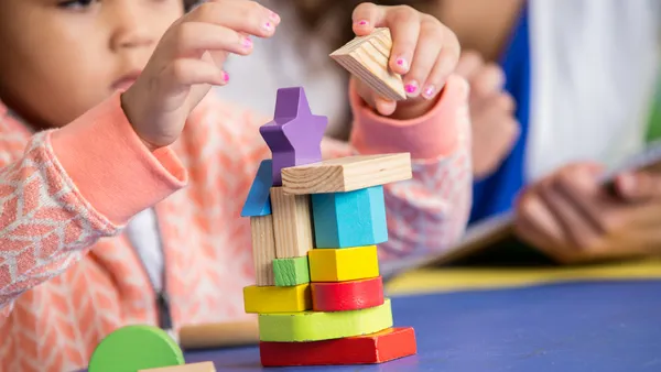 A toddler uses their hands to build blocks on a table in a classroom