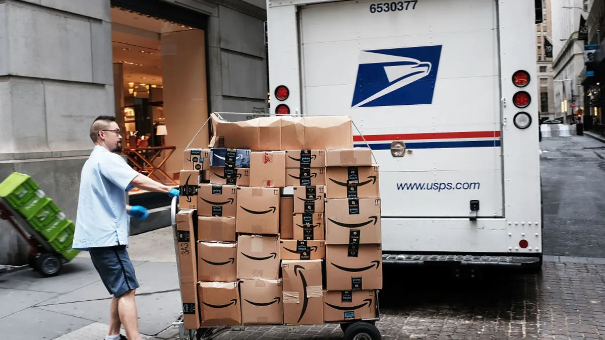 A U.S. Postal Service worker moves a cart of Amazon boxes behind a vehicle on the street.