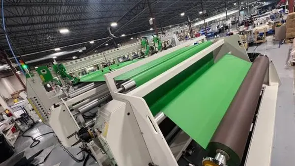 A machine manufactures green plastic fabric