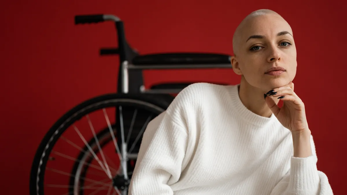 A person looks into the camera with a wheelchair behind them