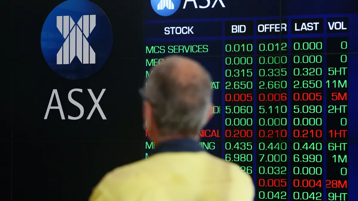 A person stands in front of an electronic board displaying stock information at the Australian Securities Exchange.