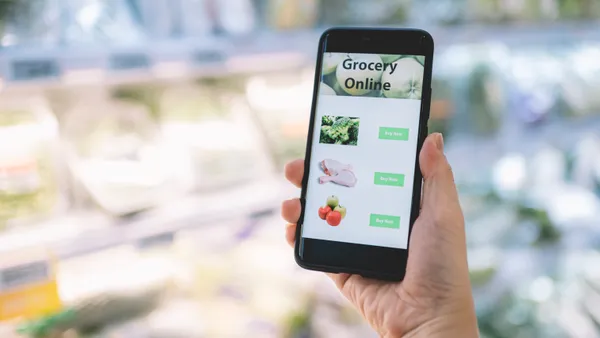 Close-up of a hand holding a phone with a grocery app open while inside a supermarket.