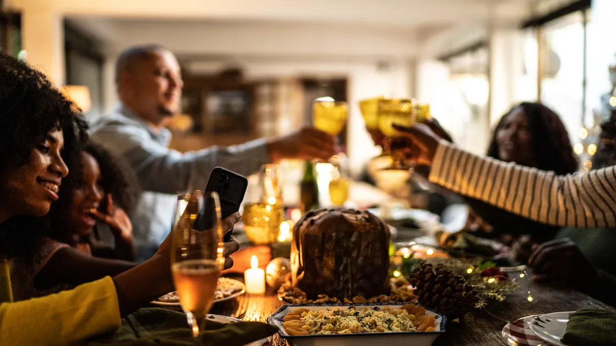 A person on a video call/filming/taking photos of a family toasting for a holiday dinner at home.