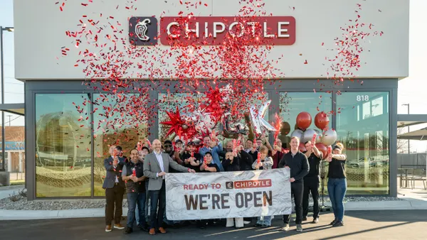 An image of a group of people holding balloons and launching confetti. They are in front of a white building with a sign that says Chipotle.