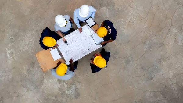 An aerial view of a group of people in construction hard hats having a meeting over plans.