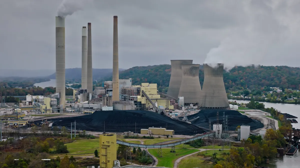 A power plant with stacks of coal sits at a bend in a river.