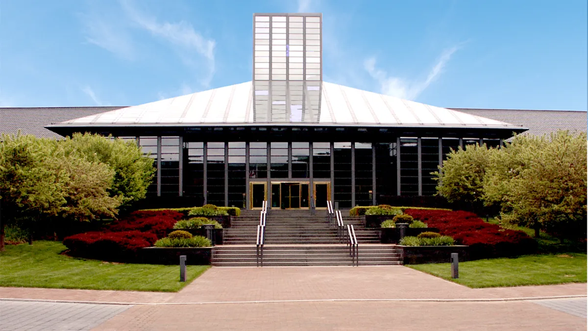 A glass building with green and brown-reddish landscape on its left and right, and an entry way in the center.