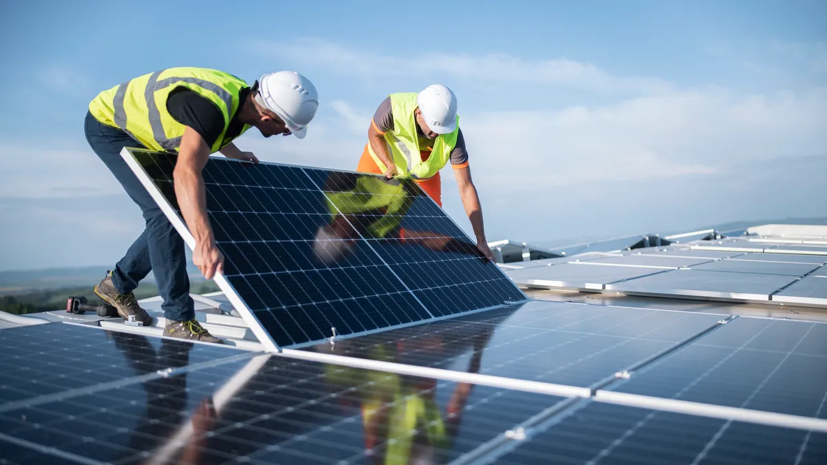 Team of two engineers installing solar panels on roof.