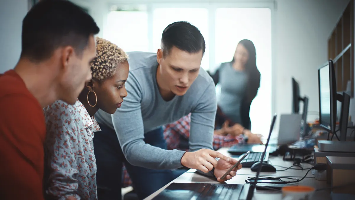 Closeup side view of group of mid 20's mobile application developers testing the code and fixing the issues.