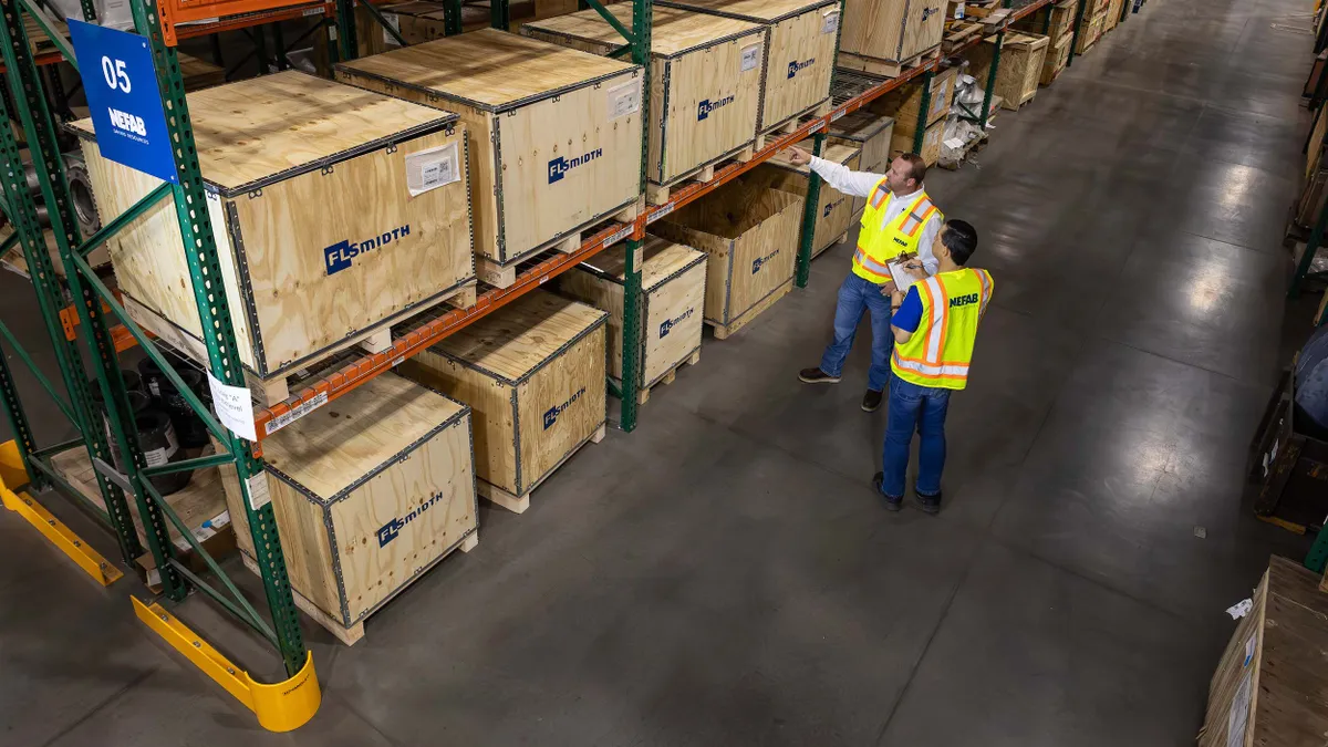 Two people in yellow safety vests stand in a Nefab warehouse with wooden crates