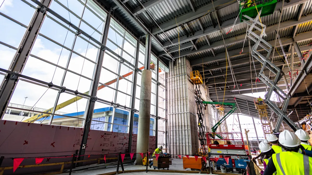 Construction workers move among equipment in a lofty airport terminal