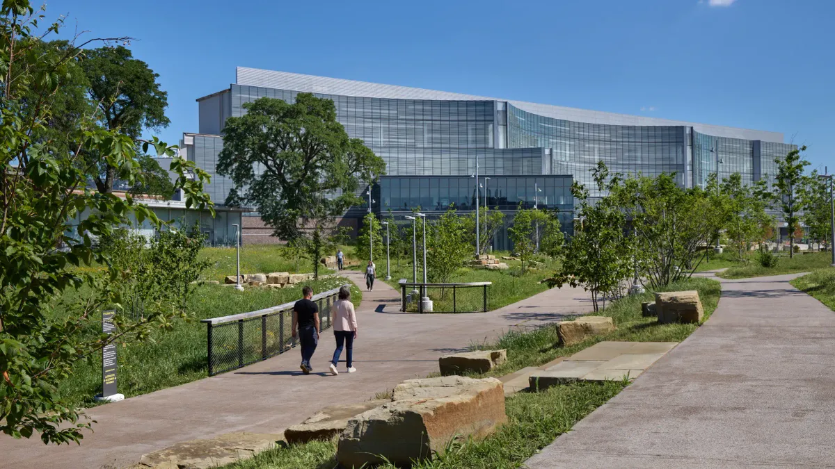 People walking on pedestrian pathways in green space surrounding Ford's new global headquarters, which is visible in the background.