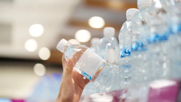 A hand reaches for a plastic water bottle from a shelf