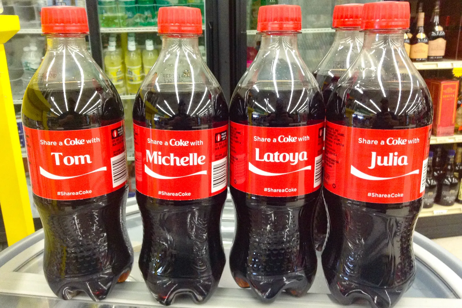 Four single-serving bottles of Coca-Cola with red labels that are identical except for the names Tom, Michelle, Latoya and Julia.