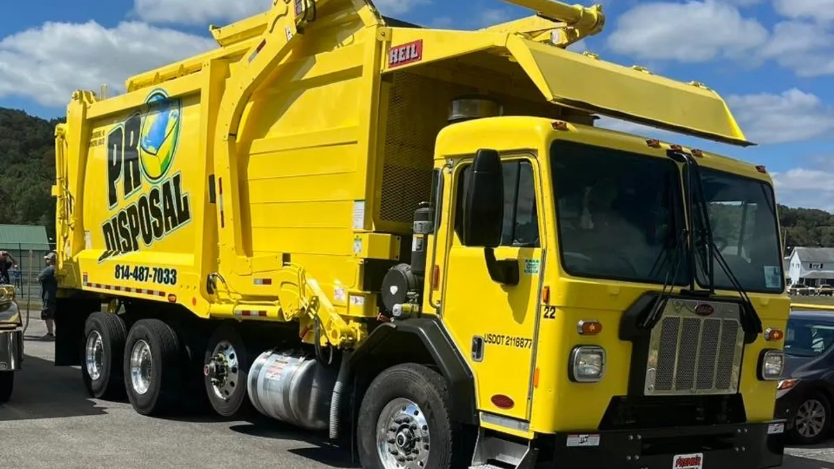 A yellow Pro Disposal truck is parked in a field