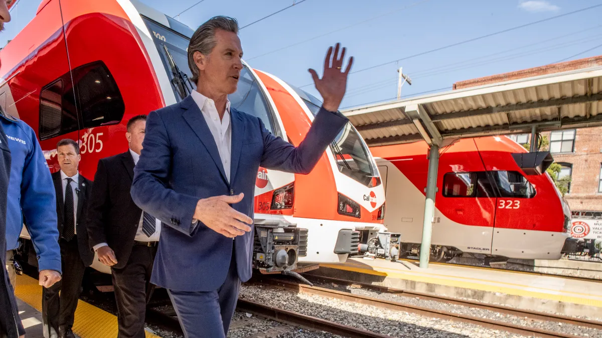 California Gov. Gavin Newsom and others walk past a brightly-painted electric commuter train.