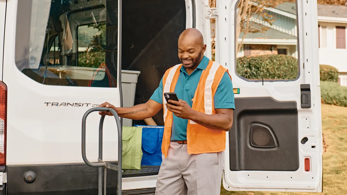 Delivery man checking his phone infront of delivery van