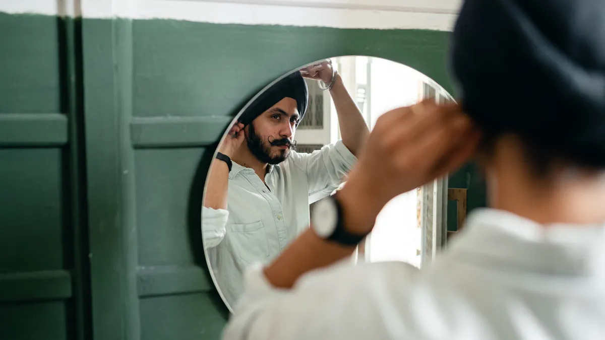 A bearded brown man looks in the mirror