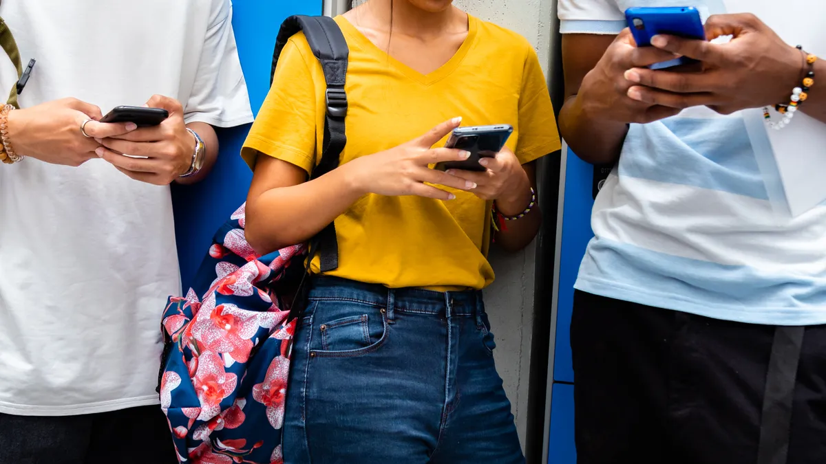 Three high school students look at their cell phones outside of a school building.