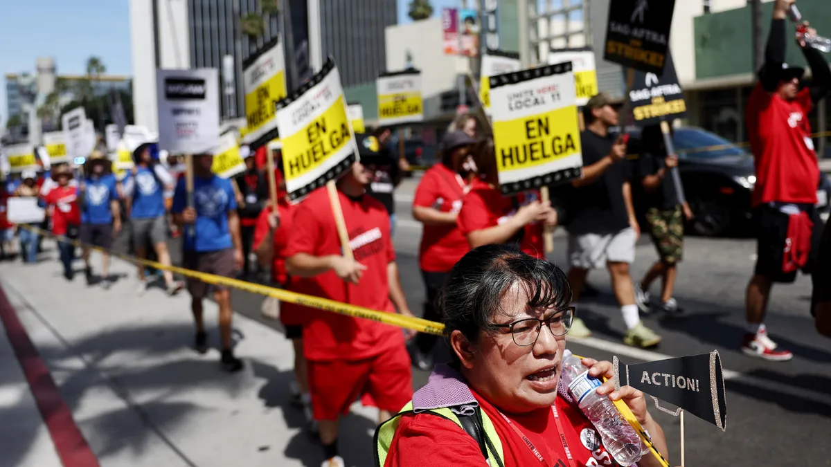 Unite Here workers in red T-shirts hold picket signs as they march along Sunset Boulevard.