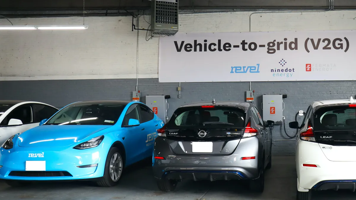 Several electric vehicles are parked in a garage under a sign that reads "Vehicle-to-grid (V2G"