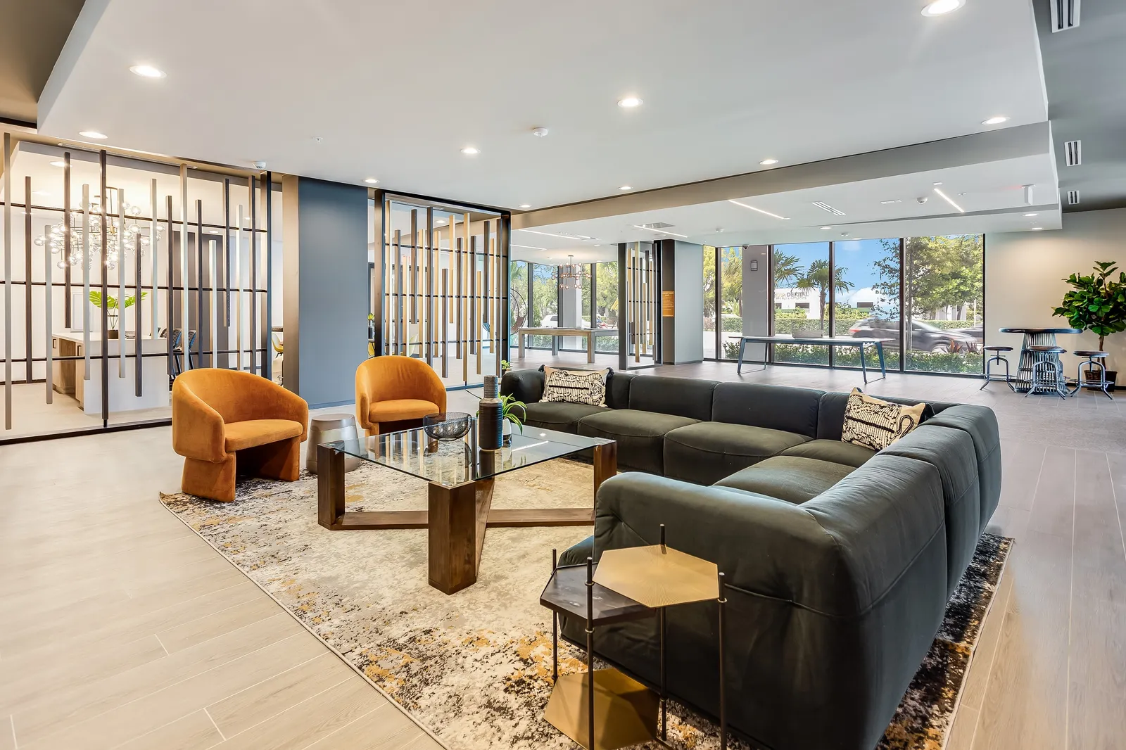 An apartment clubroom with a black sectional couch and floor to ceiling windows.