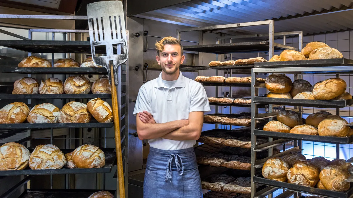 baker posing in his bakery bakehouse in the early morning between fresh baked artisan bread