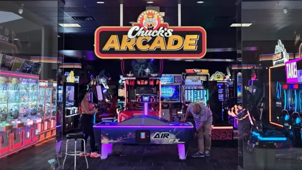 An image of an tabletop air hockey game in the center of a room with various arcade games. Above the air hockey game a sign says "Chuck's Arcade"