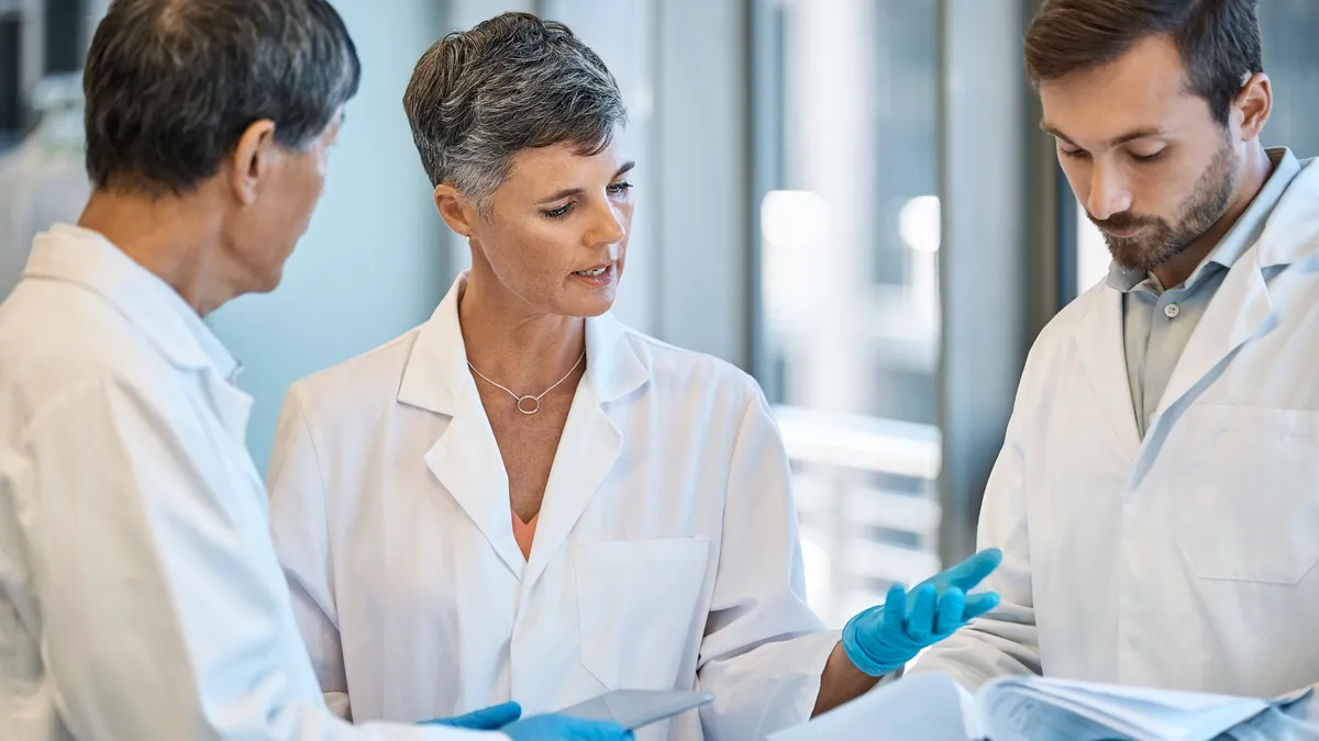 Female healthcare worker discussing over medical record with colleagues. Scientists are planning during meeting in laboratory.